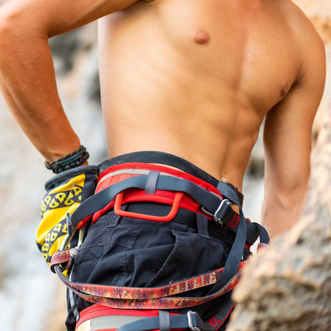 A shirtless man wearing climbing gear and showing his smooth hair-free chest and abs from men's laser hair removal.